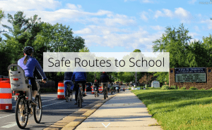 A photo of students and parents biking in the road with a barrier of traffic cones to protect them from passing vehicles during a safe routes to school demo project. A opaque white bar with black text reads "Safe Routes to School" overtop of the photo.