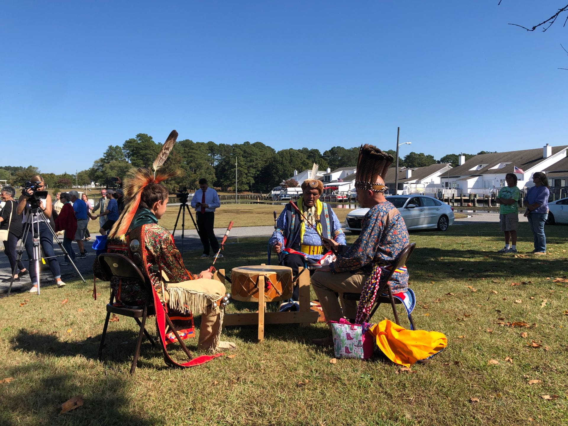 A group of indigenous people sit around a drum circle in traditional outfits. 