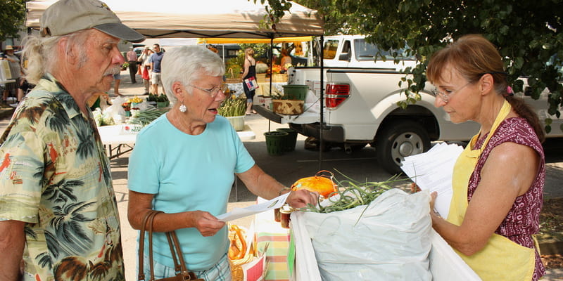 Senior community members negotiate at a vendor's table at a farmers market. 