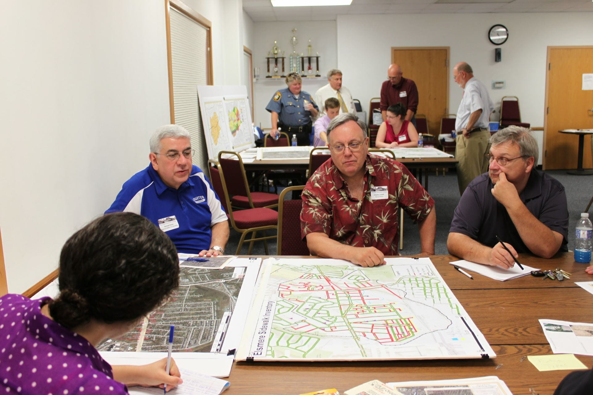 Community members sit around a table covered by a large map and converse. 